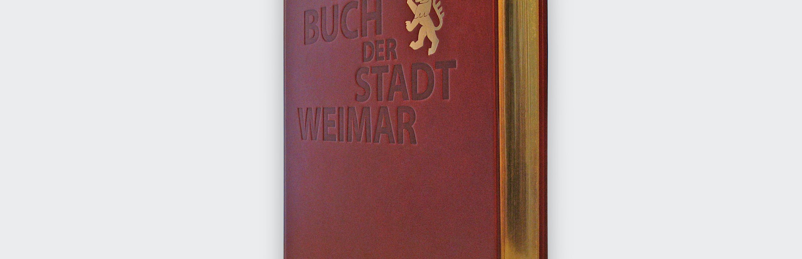 Das »Goldene Buch der Stadt Weimar« stehend aus der seitlichen Perspektive. Zu sehen ist die Prägung auf der Vorderseite und der Goldschnitt an der Seite. Das Buch wurde in der Hohlkehle fotografiert.